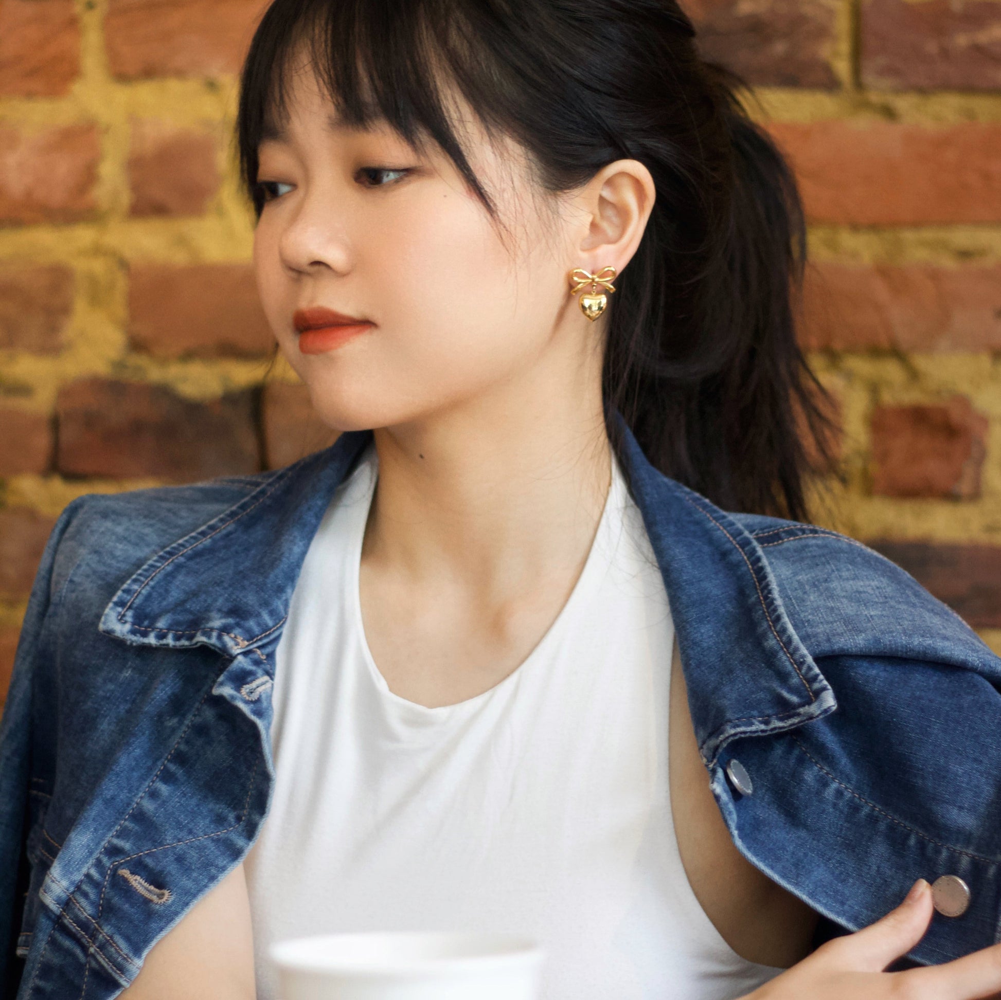 A cool girl at a coffee shop wearing heart & bow earrings 